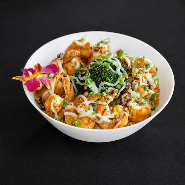 Crispy shrimp and broccoli bowl with white sauce, green onions, and a pink orchid garnish.
