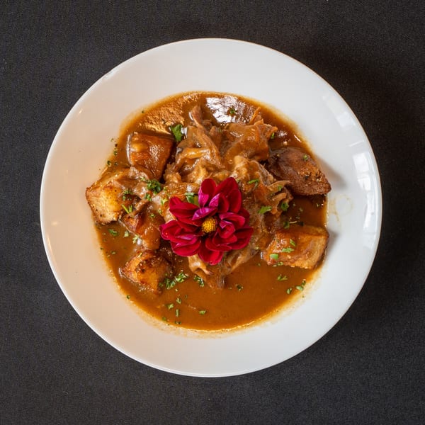 Stewed meat and potatoes in a rich brown sauce, garnished with parsley and a red flower.