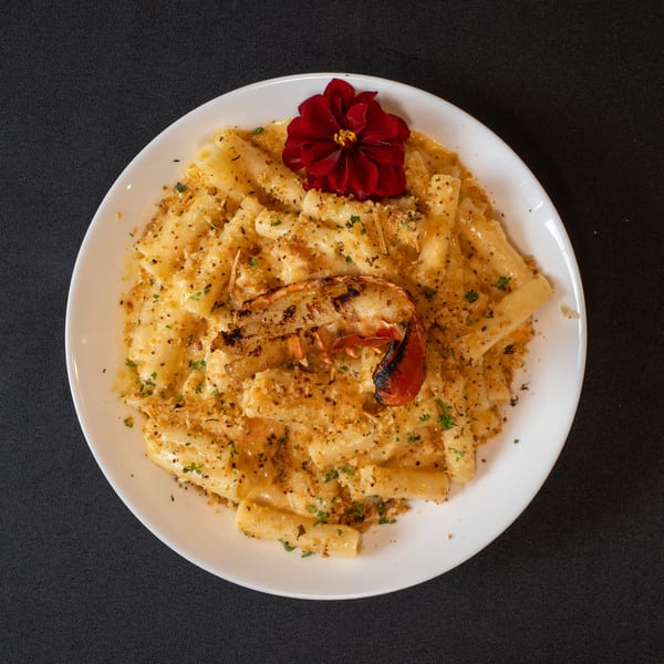 Lobster mac and cheese with a red flower garnish on a white plate.