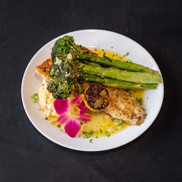Grilled fish with asparagus, broccoli, mashed potatoes, lemon, and an orchid garnish.