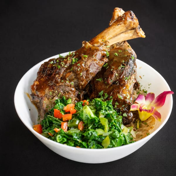 Two braised short ribs with gravy, green vegetables, and a pink orchid in a white bowl.