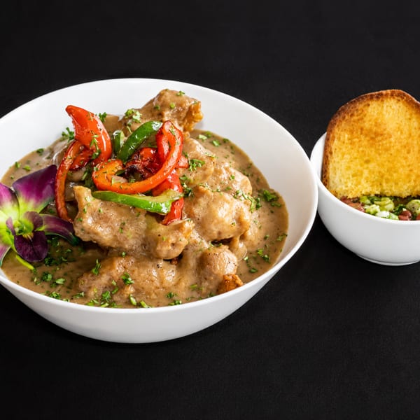 Creamy chicken dish with peppers and an orchid, alongside a bowl of beans and toast.