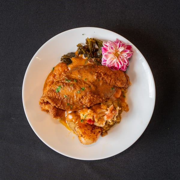 Fried fish, shrimp, and scallops with collard greens and a pink flower on a white plate.