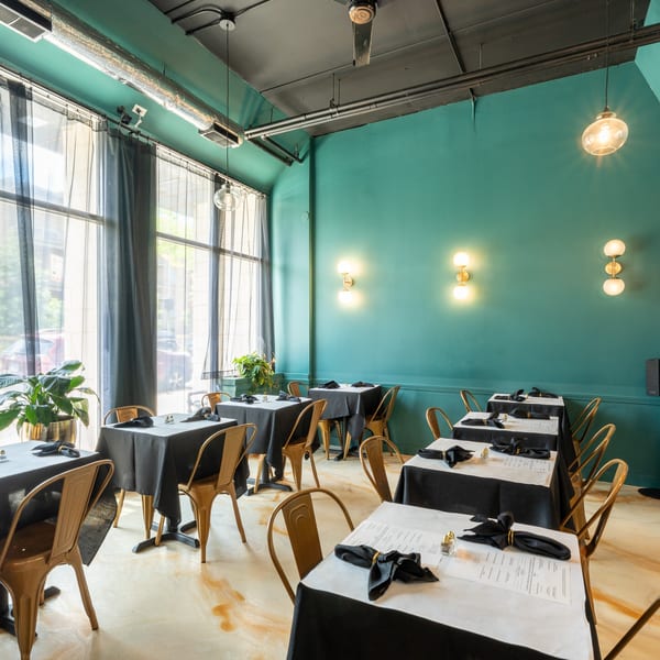 Restaurant dining room with teal walls, black tablecloths, gold chairs, and large windows.