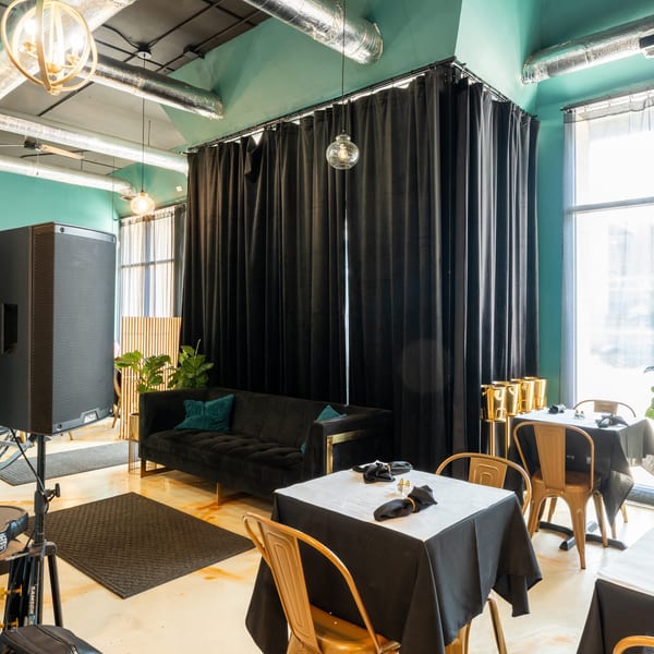Restaurant interior with black velvet curtains, a sofa, gold chairs, and tables with black tablecloths.