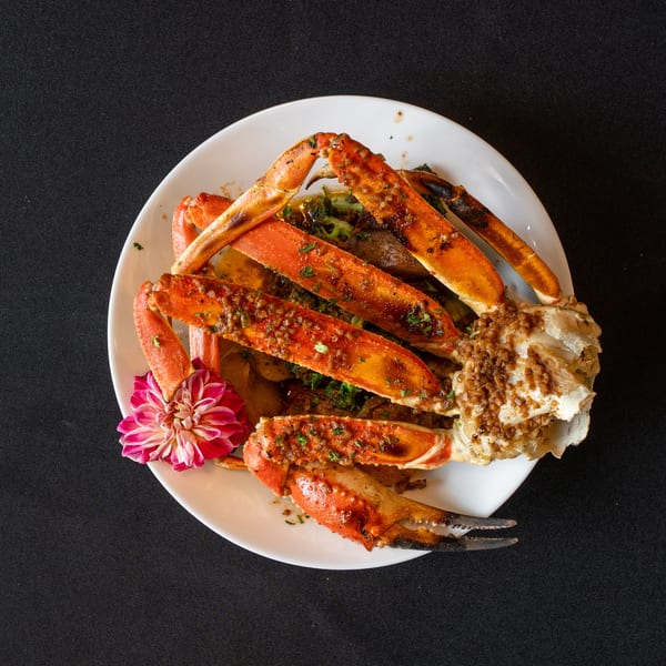 A white plate with crab legs, broccoli, and potatoes, garnished with a pink flower.