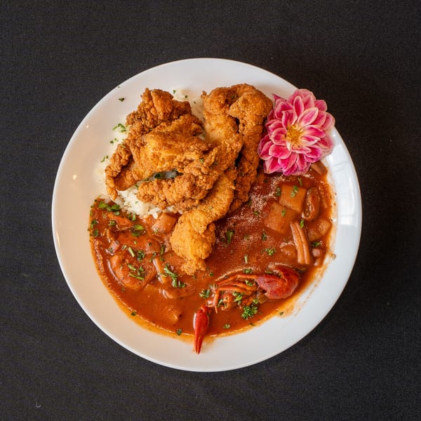 Fried chicken tenders, rice, and crawfish étouffée with a pink dahlia on a white plate.