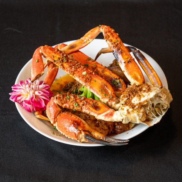A white plate holds cooked crab legs garnished with a pink and white flower.