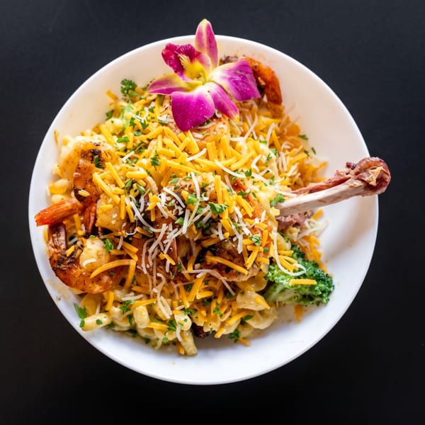 Macaroni and cheese with shrimp, chicken drumstick, broccoli, and a purple orchid garnish.