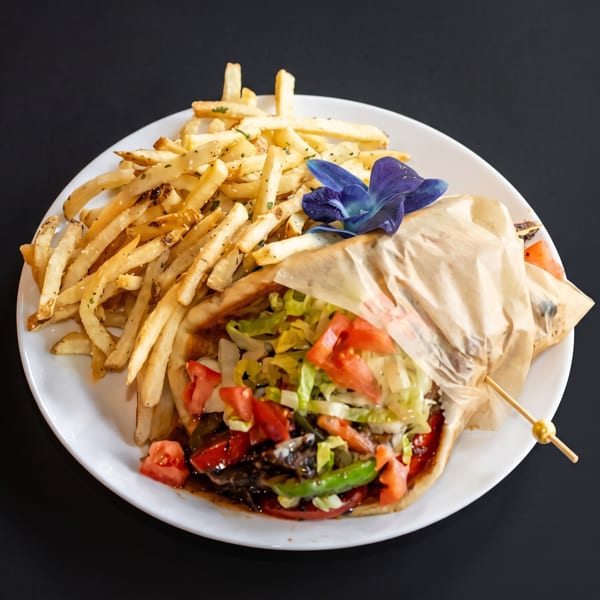 A gyro with lettuce, tomatoes, and sauce, served with a side of french fries and a blue orchid.
