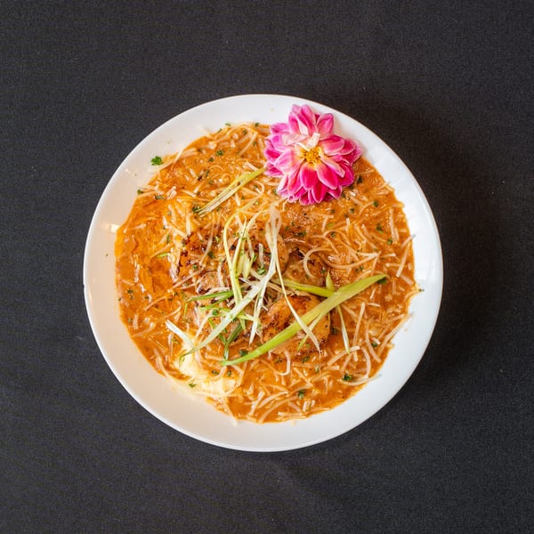 Overhead view of a white bowl filled with noodles, shrimp, and a pink flower garnish.