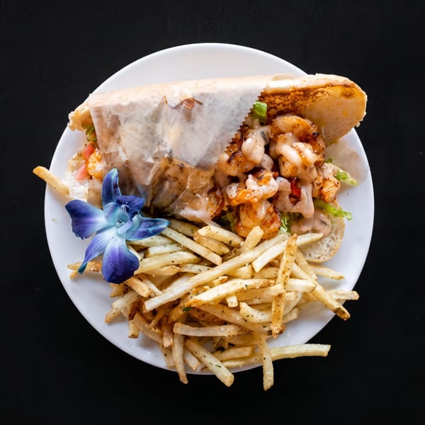 Shrimp po'boy sandwich with fries and a blue orchid on a white plate.