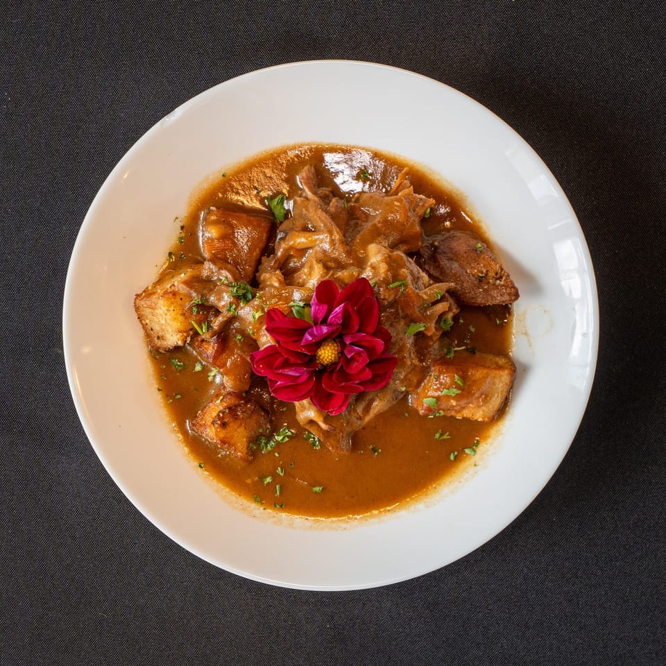 Hearty stew with meat and potatoes in a rich brown sauce, garnished with a red flower.