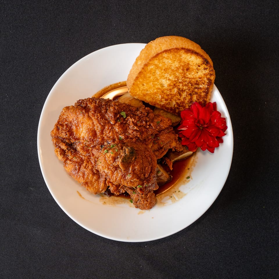 Crispy fried chicken with gravy, toasted bread, and a red flower on a white plate.