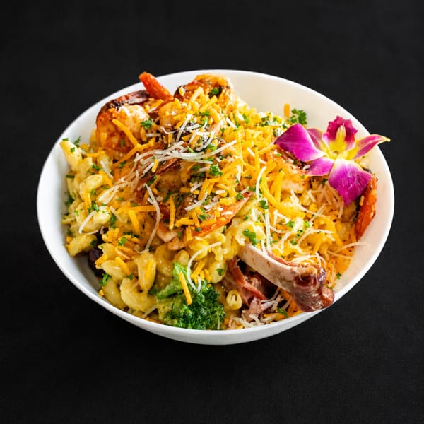 Macaroni and cheese with shrimp, broccoli, and a rib, garnished with cheese and an orchid.