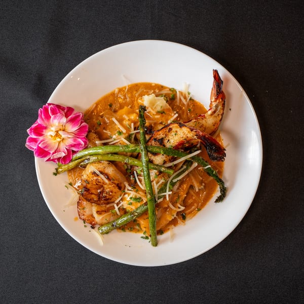 Grilled shrimp and scallops with asparagus and pasta in a creamy orange sauce, garnished with a pink flower.