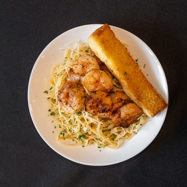 Grilled shrimp and pasta with shredded cheese and parsley, served with a slice of garlic bread.