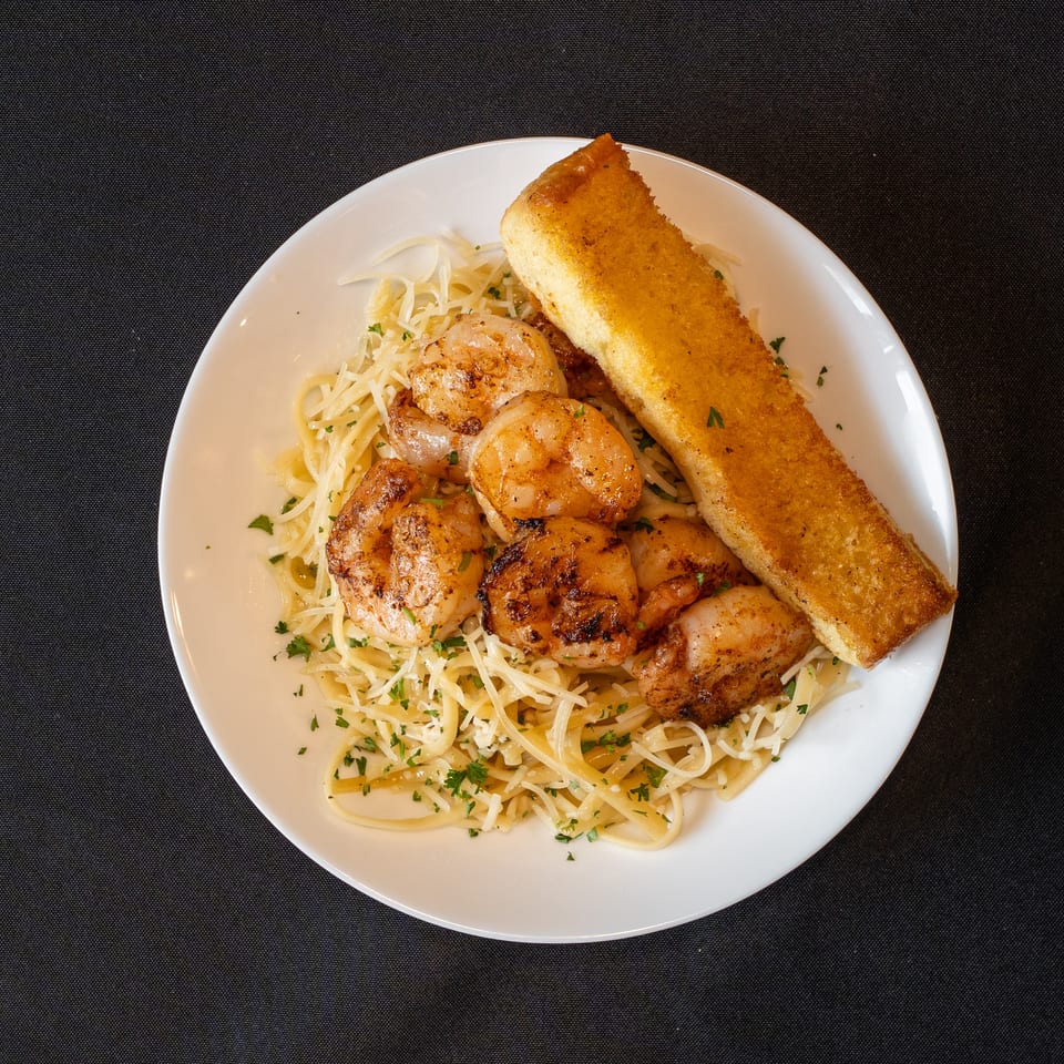 Grilled shrimp and pasta with shredded cheese and parsley, served with a slice of garlic bread.