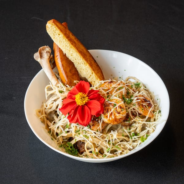 Pasta with shrimp, shredded cheese, parsley, and a red flower, served with bread and a bone.