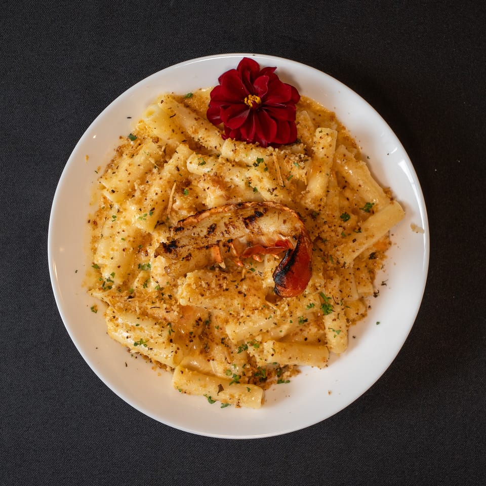 Lobster mac and cheese with a grilled lobster tail and a red flower garnish.