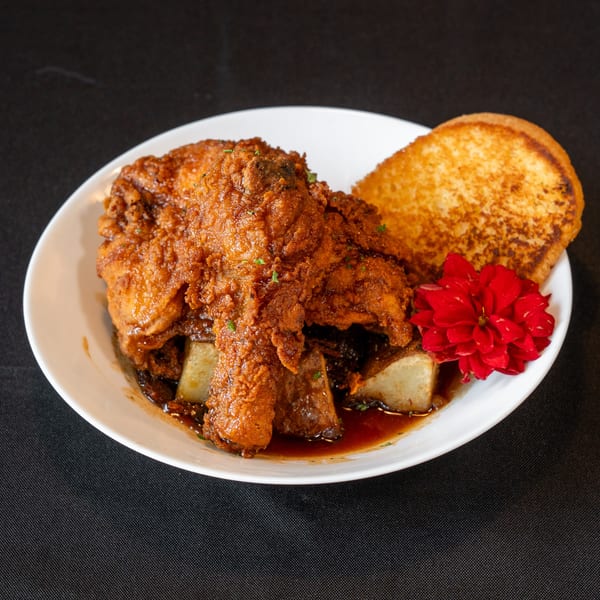Crispy fried chicken with potatoes and gravy, garnished with a red flower and toast.