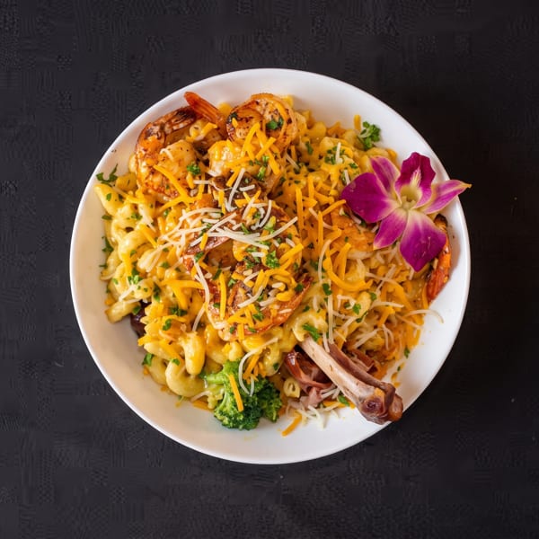 Macaroni and cheese with shrimp, broccoli, a turkey leg, and a purple orchid garnish.